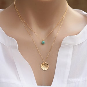 May include: A gold layered necklace with a turquoise stone pendant and a hammered gold disc pendant.