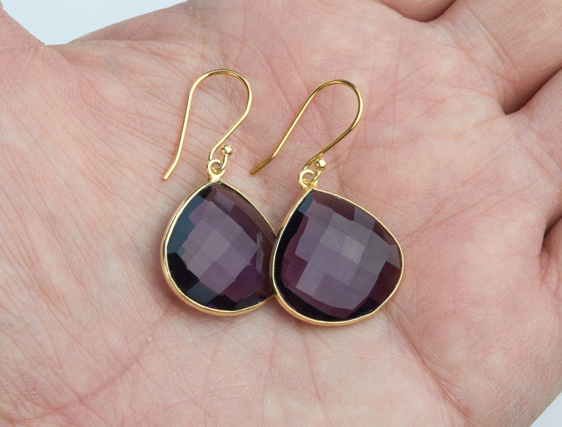 May include: A pair of gold dangle earrings with teardrop-shaped amethyst gemstones.