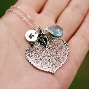 Puede incluir: Un collar de plata con un delicado colgante de hoja de plata, un peque&ntilde;o disco de plata con la inicial "L" grabada y una piedra preciosa azul.