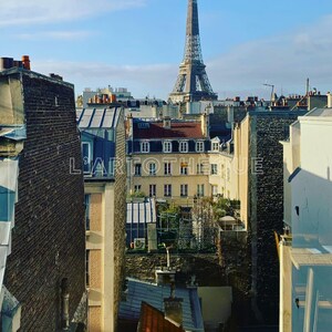 Peut inclure: Vue de la tour Eiffel depuis un toit à Paris, France. La tour est au loin, et l'avant-plan est rempli des toits des bâtiments voisins. Les bâtiments sont en brique et en pierre, et ils présentent une variété de styles architecturaux différents.