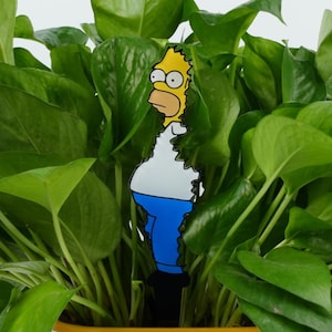 May include: A yellow cartoon character with blue jeans and a white shirt is peeking out from behind a potted green plant.