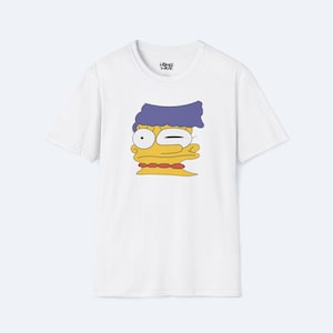May include: White t-shirt with a cartoon depiction of Marge Simpson winking. The design includes her blue hair, yellow skin, and red necklace. The shirt has the text "HOMER WEAR" on the upper right side.