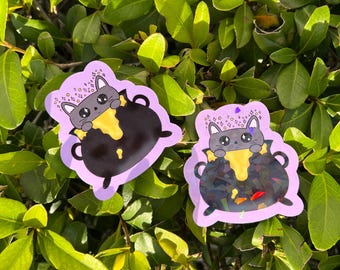 May include: Two stickers featuring a gray cat with a cauldron. The cat is pouring yellow liquid from the cauldron. The stickers have a purple border and are set against a background of green leaves.