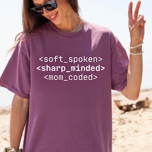 May include: Purple t-shirt with white text that reads "<soft_spoken> <sharp_minded> <mom_coded>"