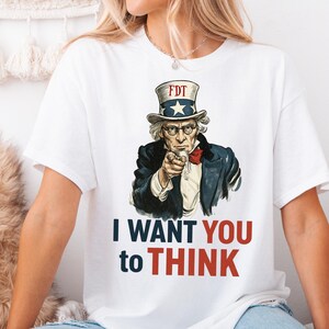 May include: White t-shirt with a graphic of Uncle Sam pointing and saying "I WANT YOU to THINK". The graphic is in a vintage style and Uncle Sam is wearing a red, white, and blue hat with the letters "FDT" on it.