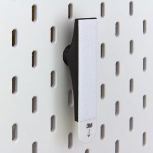 Pu&ograve; includere: Un gancio nero per pannello forato con una striscia adesiva bianca, progettato per il montaggio su un pannello forato bianco. Il gancio &egrave; in plastica nera e ha un design curvo. La striscia adesiva presenta il logo "3M" e una freccia che indica la direzione di applicazione.
