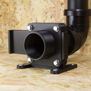 Könnte beinhalten: Ein schwarzes Industrieteil mit zylindrischer Öffnung und gebogenem Rohranschluss. Befestigt mit silbernen Schrauben, ruht es auf einer Holzoberfläche. Das Design deutet auf eine funktionale, mechanische Anwendung hin.