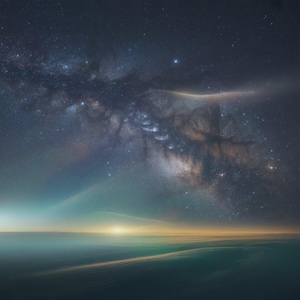 May include: A celestial landscape featuring a vibrant night sky filled with stars and the Milky Way. The scene transitions to a horizon with a soft, golden glow, suggesting a sunrise or sunset. The overall color palette is dominated by blues, greens, and golds.