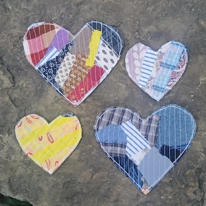 May include: Four heart-shaped fabric patches featuring various textile patterns and colors. The largest heart displays a mix of plaid, floral, and solid strips. A smaller heart features yellow fabric with red shapes, while others show blue, white, and plaid designs.