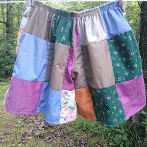 May include: Patchwork shorts in a variety of colors, including purple, blue, green, and brown. The shorts are made of different fabrics and patterns, including floral and solid colors. The shorts are hanging on a clothesline.