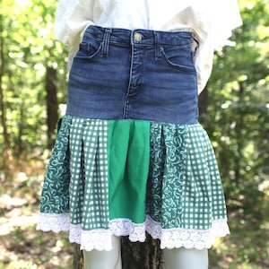 May include: A denim skirt with a green and white patterned skirt. The skirt has a denim waistband and a green fabric panel in the centre. The skirt has a white lace trim at the bottom.