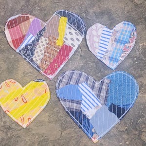 Puede incluir: Cuatro parches de tela en forma de corazón con varios patrones textiles. Un corazón es principalmente amarillo con formas naranjas, mientras que los otros están construidos con múltiples tiras de tela a cuadros, rayas y flores en tonos azul, rojo y blanco.