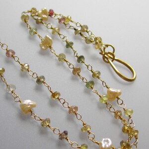 May include: Delicate gold necklace featuring a strand of small, colorful gemstones and irregular pearls. The necklace has a gold clasp. The gemstones are in shades of yellow, green, pink, and brown.