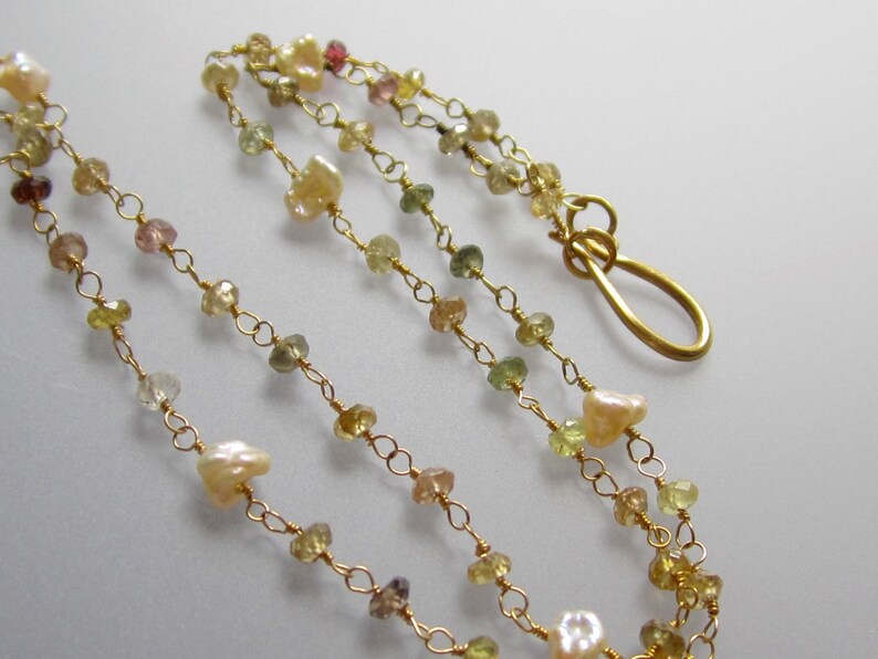 May include: Delicate gold necklace featuring a strand of small, colorful gemstones and irregular pearls. The necklace has a gold clasp. The gemstones are in shades of yellow, green, pink, and brown.