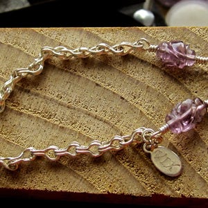 May include: A silver chain bracelet with two purple amethyst beads and a silver charm with the word "ALEX" engraved on it.