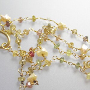 May include: A delicate necklace featuring multiple strands of gold wire, adorned with small, colorful gemstones in shades of yellow, green, and pink. The necklace also includes several creamy white pearls and a gold-colored hook clasp.
