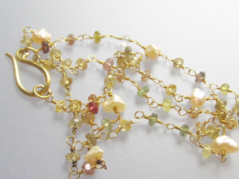 May include: A delicate necklace featuring multiple strands of gold wire, adorned with small, colorful gemstones in shades of yellow, green, and pink. The necklace also includes several creamy white pearls and a gold-colored hook clasp.