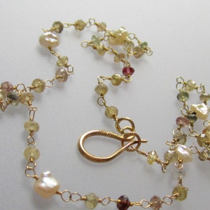 May include: Delicate gold-toned necklace featuring a series of small, colorful gemstones and irregular-shaped pearls. The necklace is strung together with fine gold wire and has a gold clasp. The gemstones are in shades of yellow, pink, and brown.