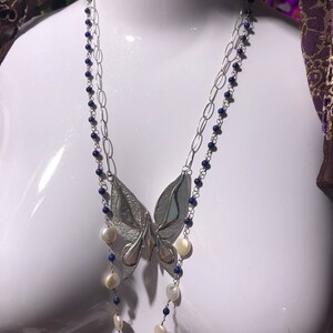 Op de afbeelding: Een zilveren ketting met een vlinder hanger, een gelaagde ketting en blauwe en witte kralen.