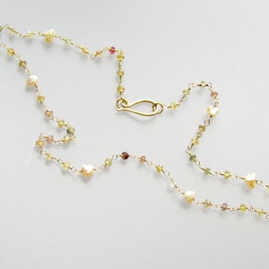 May include: Delicate gold necklace featuring small, colorful gemstones and irregular pearls. The necklace has a delicate chain and a gold-colored clasp. The gemstones are in shades of yellow, green, and pink, creating a subtle, elegant design.