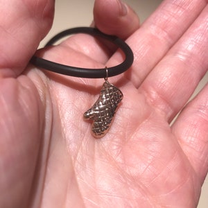 Op de afbeelding: Een zwarte siliconen armband met een gouden ovenwant-bedel.