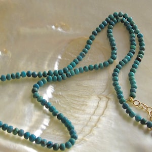 Op de afbeelding: Een turquoise kralenketting met een gouden sluiting. De ketting is gemaakt van kleine, ronde kralen en is ongeveer 46 cm lang.