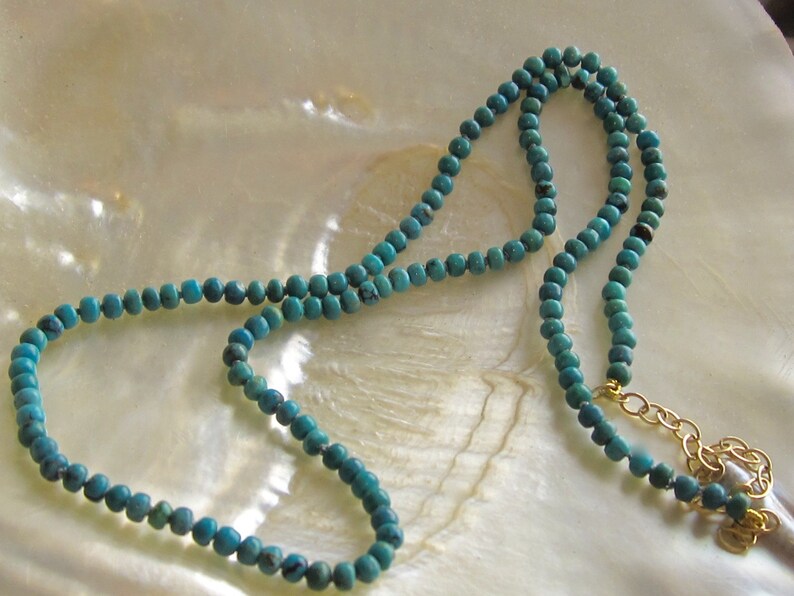 Op de afbeelding: Een turquoise kralenketting met een gouden sluiting. De ketting is gemaakt van kleine, ronde kralen en is ongeveer 46 cm lang.