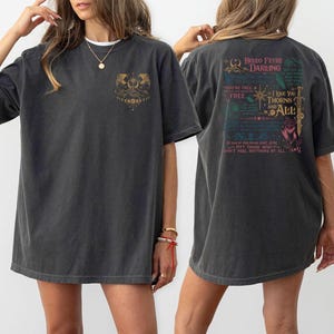 May include: Dark gray t-shirt with a front graphic of a mountain scene and a back graphic with text that reads "Hello Feyre Darling" and "I love you thorns and all". The shirt is a casual, oversized fit.