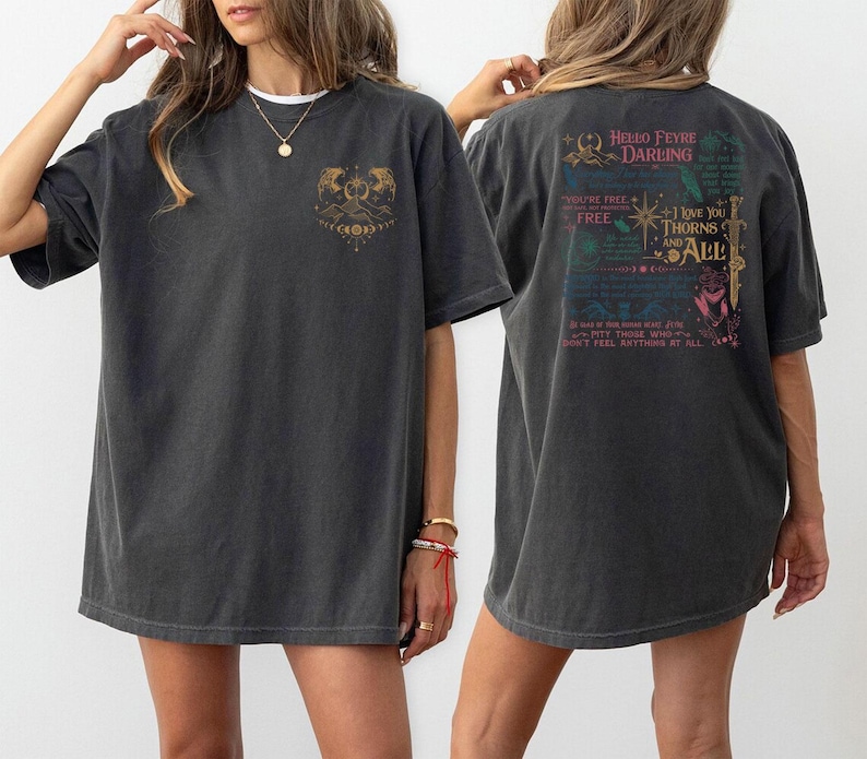 May include: Dark gray t-shirt with a front graphic of a mountain scene and a back graphic with text that reads "Hello Feyre Darling" and "I love you thorns and all". The shirt is a casual, oversized fit.