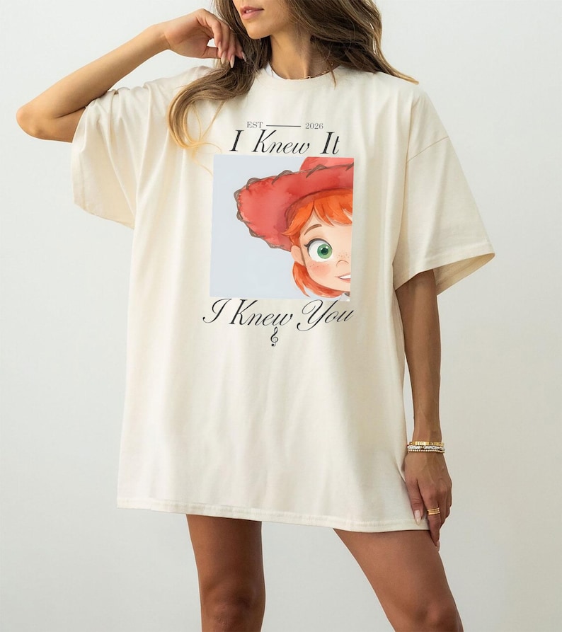 May include: An oversized cream-colored t-shirt featuring a graphic print of a cartoon character with red hair and a red hat. The text "EST 2026 I Knew It" appears above the graphic, and the text "I Knew You" is printed below the illustration.