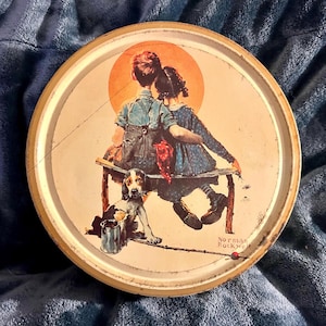 May include: Round metal tray with a painted illustration featuring two children sitting on a bench, a dog, and a fishing rod. The artwork is in a vintage style, with a warm color palette and the artist's signature.