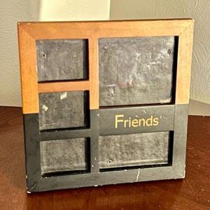 May include: A multi-photo picture frame with a wooden top and a black base. The word "Friends" is printed in gold on the base. The frame has four photo openings of varying sizes.