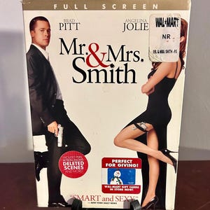 Peut inclure: DVD du film "Mr. & Mrs. Smith" avec Brad Pitt et Angelina Jolie. La couverture présente le titre en rouge et noir, avec du texte promotionnel et un autocollant Walmart. Format plein écran.