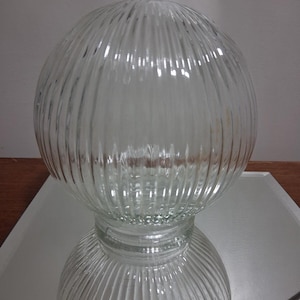 May include: A clear glass light fixture globe featuring a spherical shape with vertical ribbed detailing. The glass is transparent and textured with consistent ridges running from the top to the base, creating a uniform pattern across the surface.