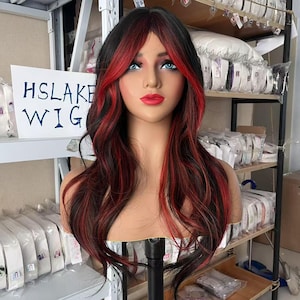 May include: A mannequin head showcasing a long, wavy wig with black and red streaks. The wig has a side parting and fringe. The mannequin has blue eyes and red lipstick. A sign in the background reads "HSLAKE WIG".