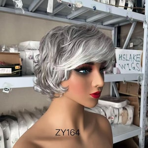 May include: A short, layered wig featuring a blend of silver, gray, and white hair tones. The hair is styled with soft waves and side-swept bangs, displayed on a smooth, tan-colored mannequin head. The text ZY164 is printed on the neck area.