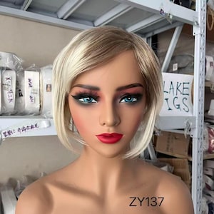 May include: A mannequin head with a short, blonde wig. The wig has a layered bob style with darker roots and lighter blonde highlights. The mannequin has blue eyes, red lipstick, and the text "ZY137" at the bottom.