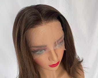 May include: A brown wig with a natural-looking hairline and a lace front. The wig features a blend of brown and lighter highlights, creating a dimensional effect. The hair is styled in a shoulder-length cut.