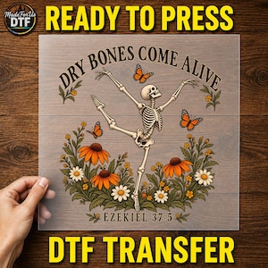May include: A transparent DTF transfer sheet featuring a skeleton in a dancing pose surrounded by orange flowers and monarch butterflies. The text reads DRY BONES COME ALIVE at the top and EZEKIEL 37:5 at the bottom in a dark brown font.