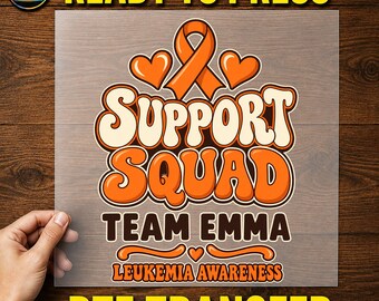 May include: A clear DTF transfer sheet featuring an orange awareness ribbon, two hearts, and the text Support Squad, Team Emma, and Leukemia Awareness in orange, cream, and dark brown colours with a bold, rounded font style.