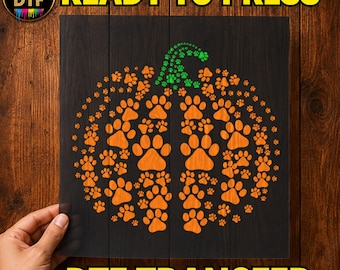 Puede incluir: Una hoja de transferencia DTF cuadrada con forma de calabaza compuesta totalmente por huellas de patas naranjas, con un tallo de huellas verdes en la parte superior. El texto READY TO PRESS y DTF TRANSFER está impreso en amarillo.