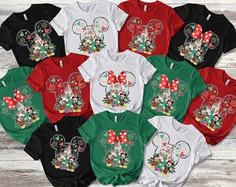 May include: A collection of short-sleeved t-shirts in black, white, red, and green, each featuring a graphic of Mickey and Minnie Mouse in front of a castle, decorated with a Christmas tree, presents, and a large red polka-dot bow.