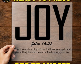 May include: A clear DTF transfer sheet featuring the word JOY in large black capital letters. Below the word is the text John 16:22 followed by the verse: Now is your time of grief, but I will see you again and you will rejoice, and no one will take away your joy.