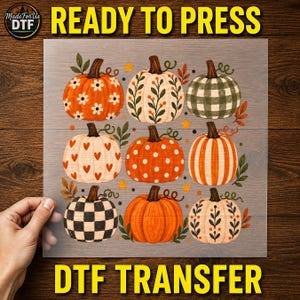 May include: A DTF transfer sheet featuring a grid of nine pumpkins with various patterns including white daisies, green gingham, red hearts, white polka dots, and orange stripes, accented with small orange stars and green leaves on a clear film.