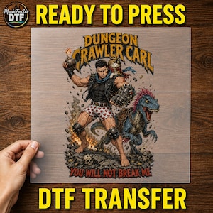 Könnte beinhalten: Ein DTF-Transferbogen mit einer grafischen Illustration eines muskulösen Mannes in Boxershorts mit Herzmuster und Lederweste, der eine Bombe hält, mit einer Katze auf der Schulter und einem blauen Dinosaurier daneben. Der Text lautet Dungeon Crawler Carl und You Will Not Break Me.