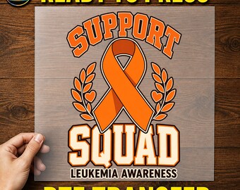 May include: A clear DTF transfer sheet featuring an orange awareness ribbon graphic with the text SUPPORT SQUAD and LEUKEMIA AWARENESS. The design includes orange laurel branches and small hearts, with the text READY TO PRESS DTF TRANSFER.