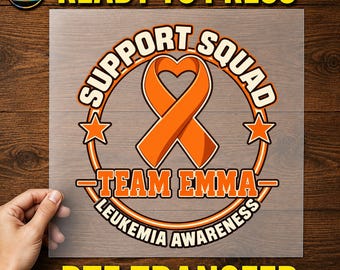 May include: A DTF transfer sheet featuring an orange awareness ribbon shaped like a heart. The design includes the text SUPPORT SQUAD, TEAM EMMA, and LEUKEMIA AWARENESS in orange and black, accented by two orange stars within a circular border.
