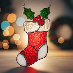 May include: Stained glass Christmas stocking ornament. The red textured body contrasts with the white toe and cuff. The top features a holly and berry design. It hangs from a silver chain.