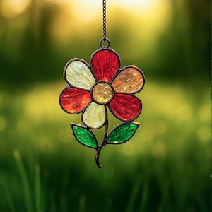 Puede incluir: Un atrapasoles de flores de vidriera con pétalos rojos, amarillos y naranjas, un centro dorado y hojas verdes. La flor está suspendida por una cadena, perfecta para la decoración de jardines o ventanas.