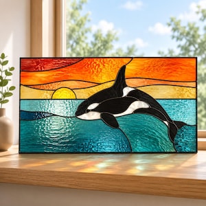 May include: A rectangular stained glass panel featuring a black and white orca whale leaping from textured blue and teal water. The background displays a vibrant sunset with horizontal bands of yellow, orange, and red glass pieces.